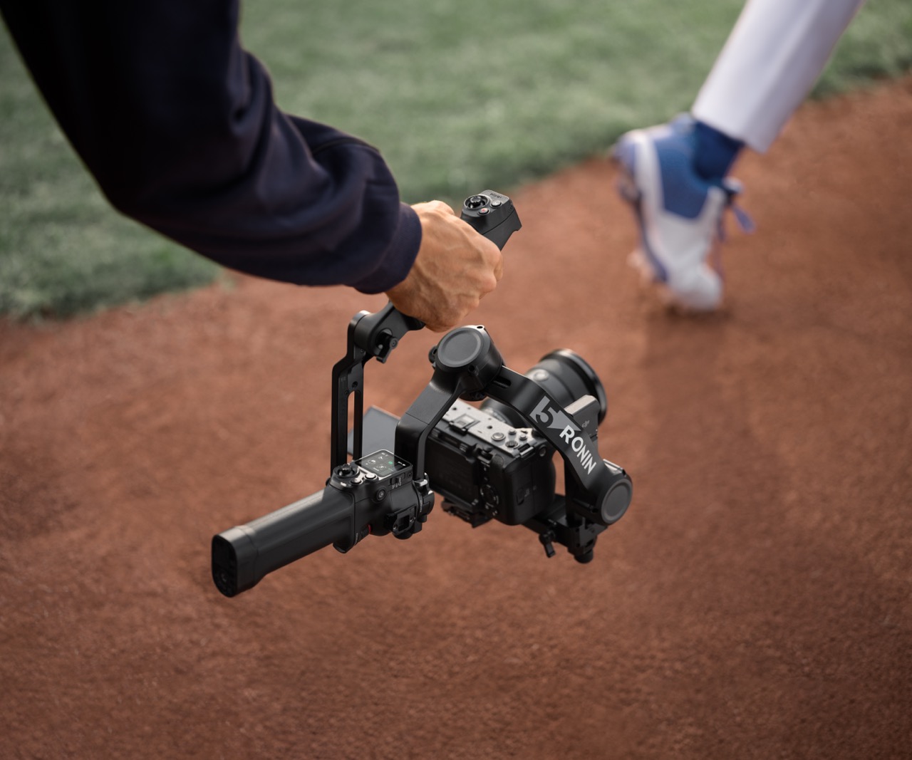 A person holding a gimbal in one hand with a camera attached, while they film the foot of a runner on a track