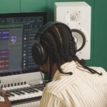 A person working on a keyboard attached to a large monitor, which shows music mixing software onscreen
