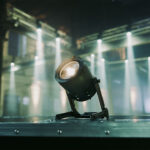 An Astera light sitting on the edge of a stage with beams of light on the set behind