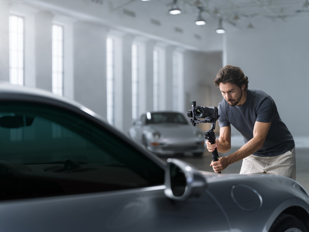 A man filming a car in a shop, using a DJI gimbal