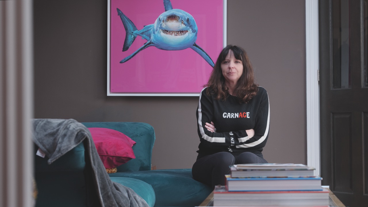 A woman sitting in a sitting area with a pink and blue print of a shark behind her