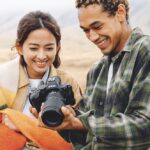 A man and woman standing in a mountainous landscapes and smiling while they look at a camera screen