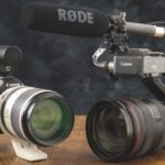 Two Canon cameras with different lenses and attachments, resting on a wooden table with a black background