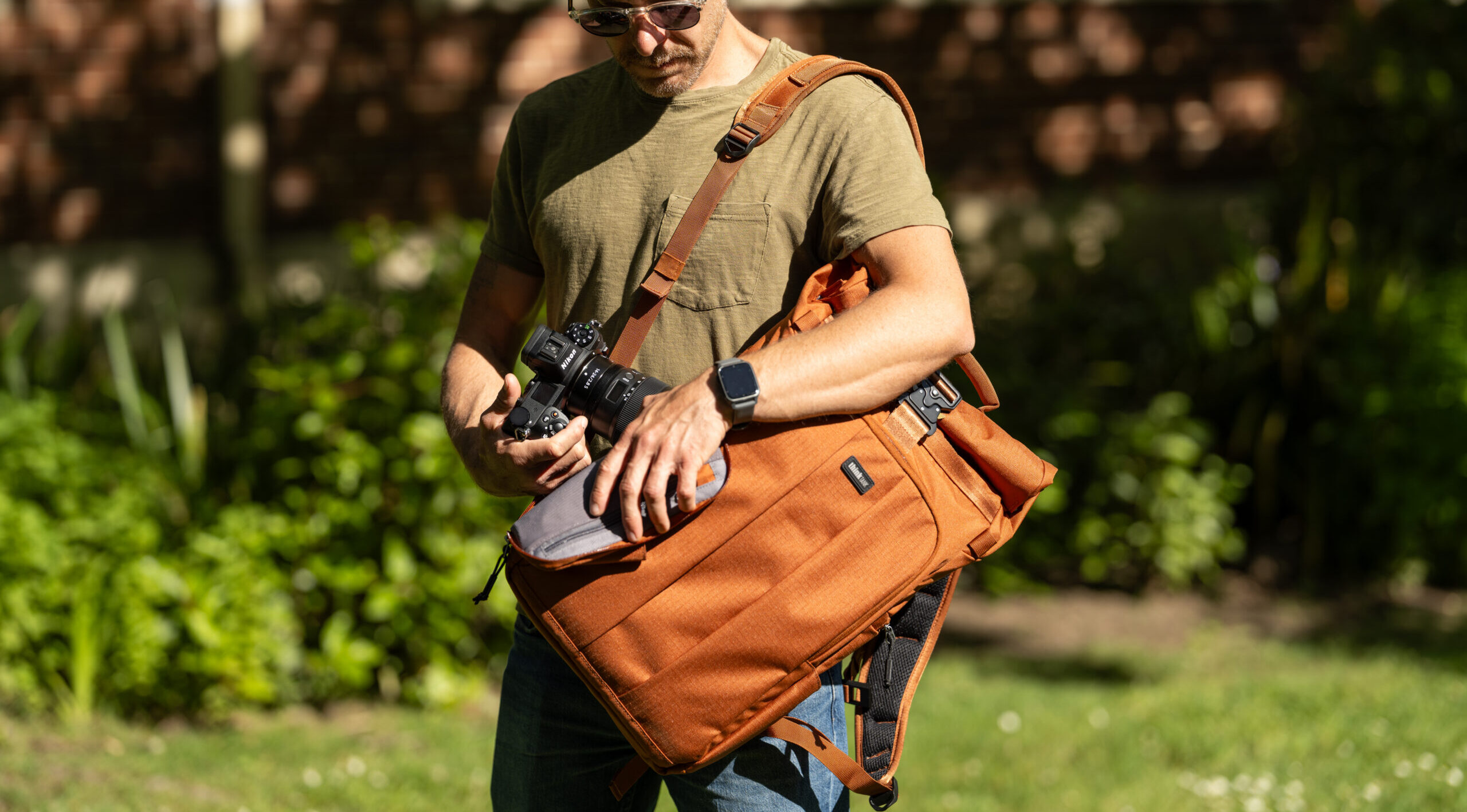 man placing camera into think tank focus point 30L rollmop backpack in rust colour way