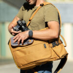 man placing camera into think tank focus point 30L rollmop backpack in golden hour colour way